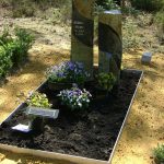 Twee zuilen van Turks Basalt als grafsteen. Tuintje met paarse violen.