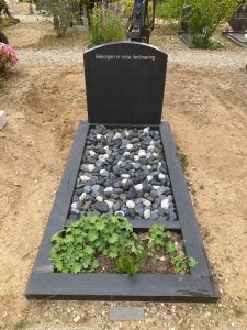 Donkere-grafsteen-met-grote-sierkeien-en-plantvak